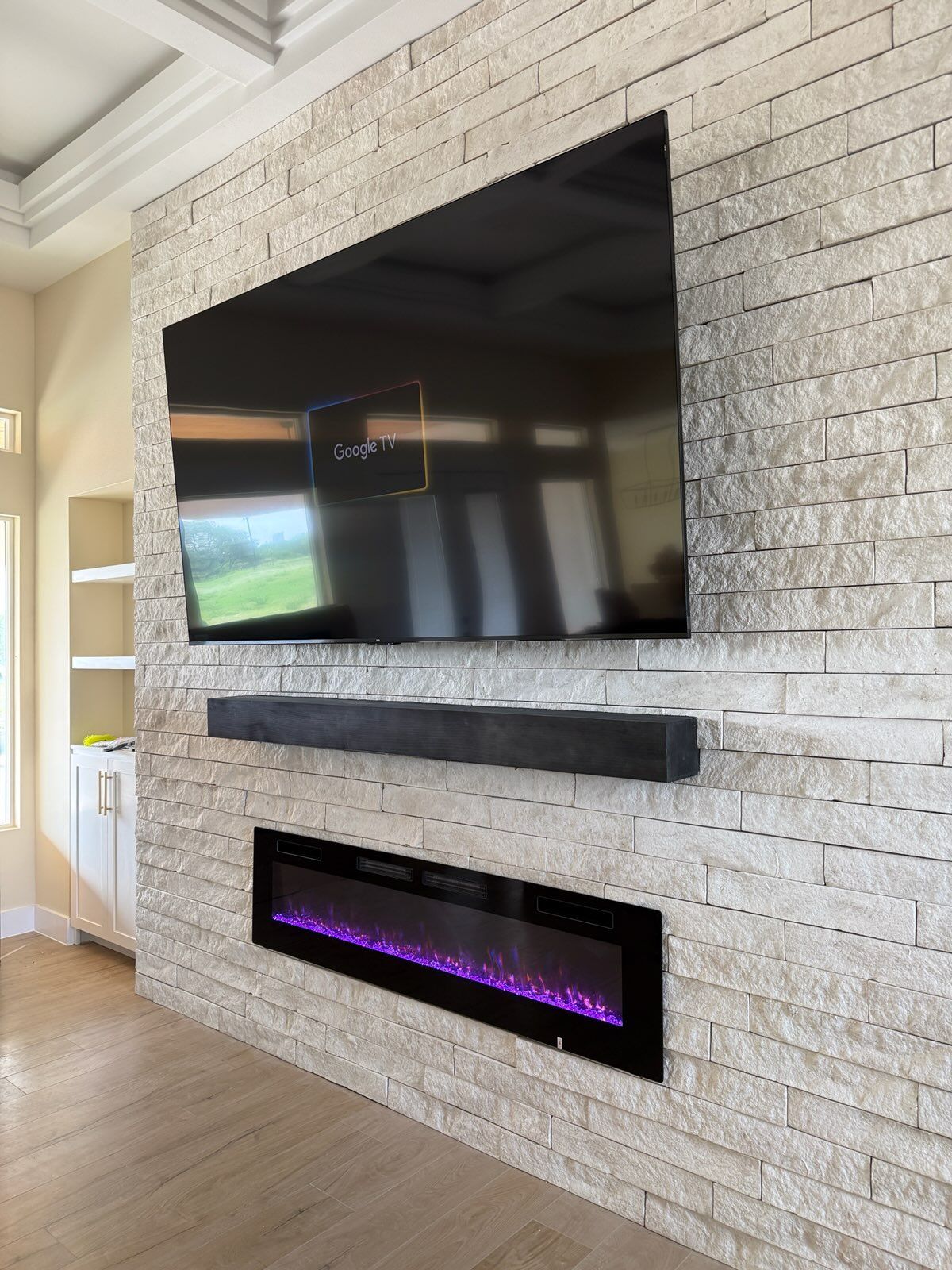 Large wall-mounted TV above a black fireplace and purple electric insert on a white stone feature wall