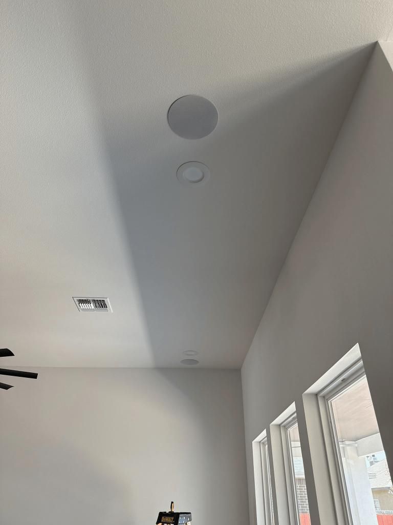 White ceiling with recessed speakers and a rectangular vent, near a window.