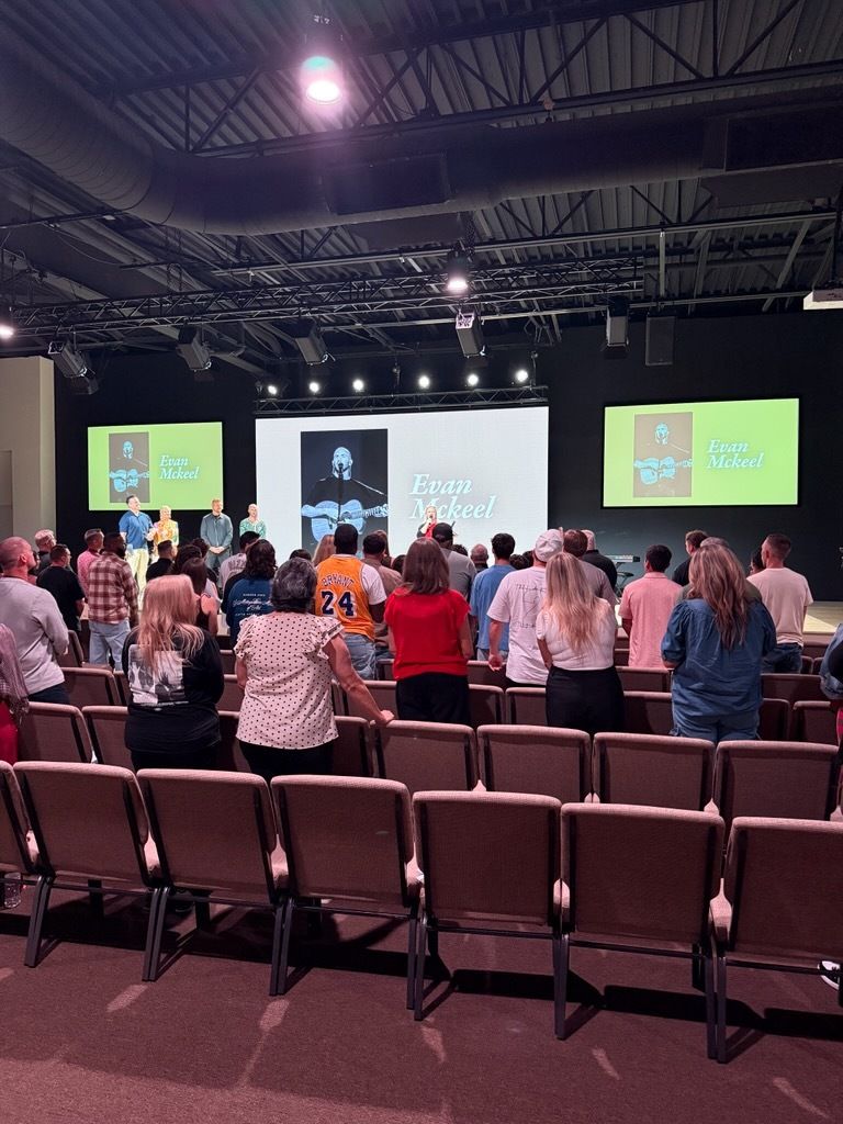 People standing and singing in a church auditorium with a stage featuring screens.