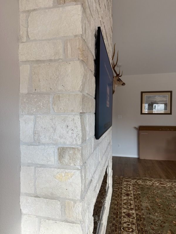 Stone fireplace with mounted TV and deer head, in a living room with rug and artwork.