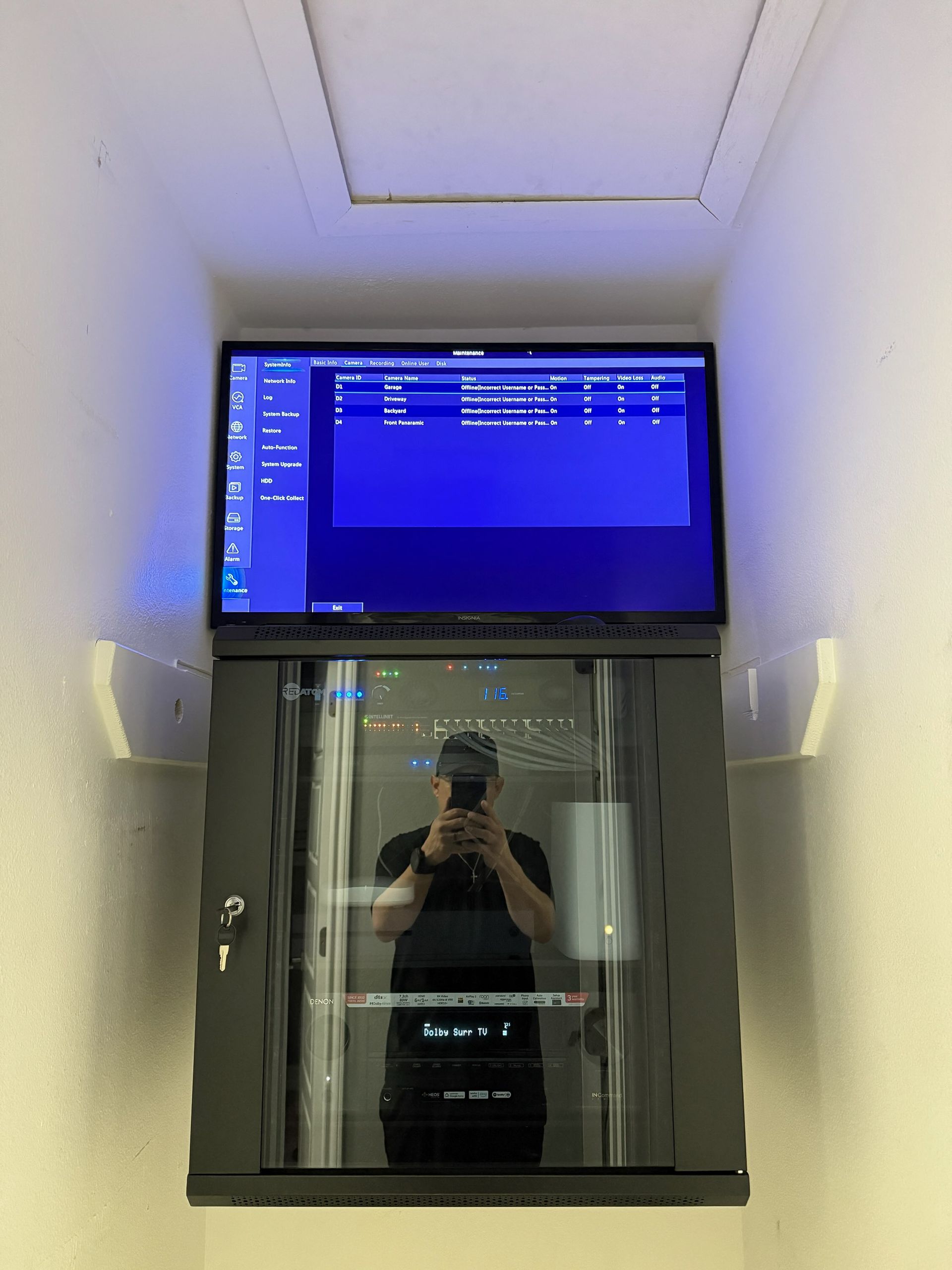 Server rack mounted in a narrow space with a monitor overhead, reflecting a person taking a photo.