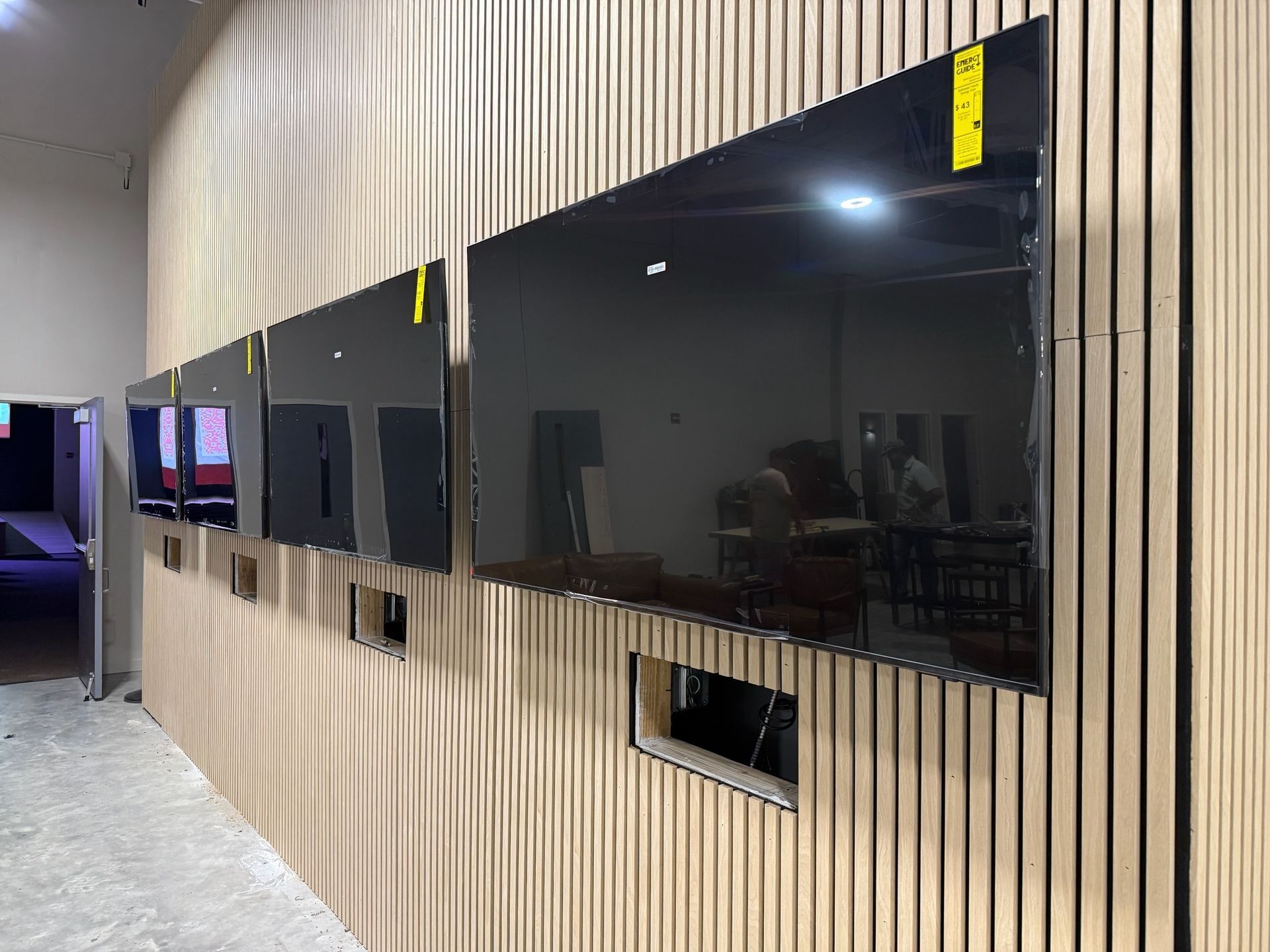Three large, black, rectangular screens mounted on a wooden-slatted wall. A room interior.