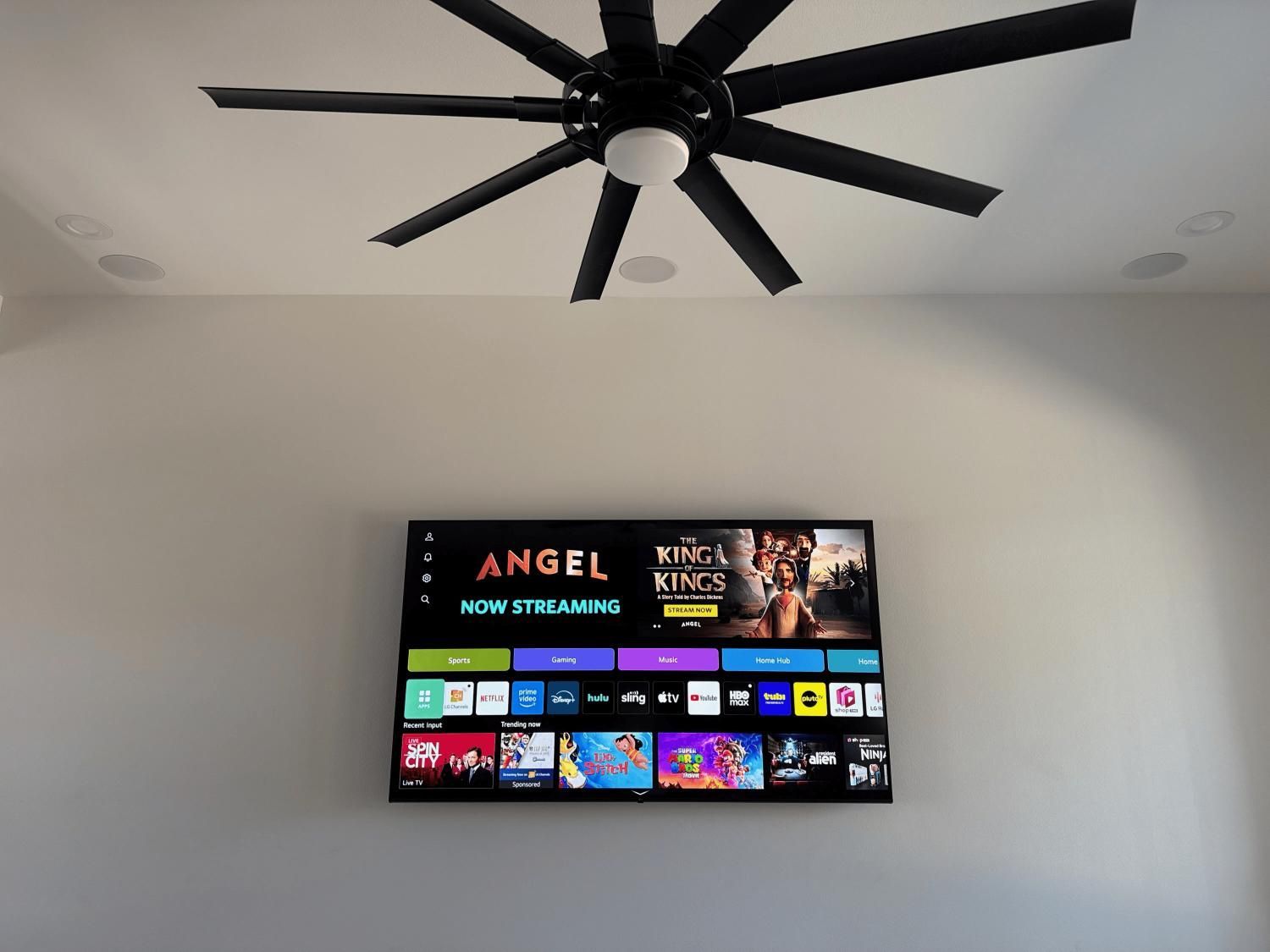 TV mounted on a wall displaying streaming service interface, beneath a ceiling fan.