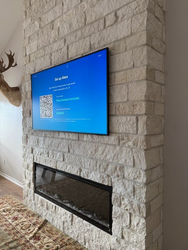 A large TV mounted above a modern fireplace on a light stone wall. Deer head on the left.