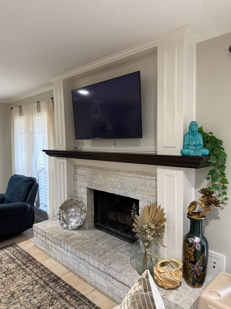 A fireplace with white-washed brick, a dark wood mantel, a mounted TV, and decorative items including a blue Buddha statue.