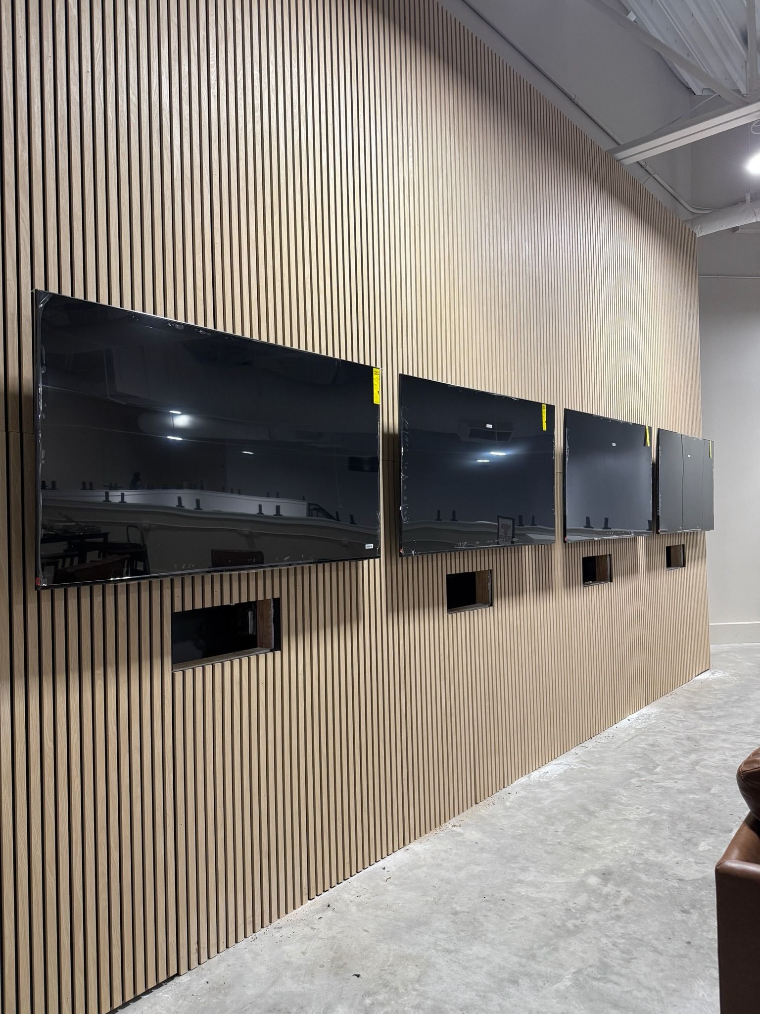 Five mounted black TVs on a wavy, wood-paneled wall. Electrical outlets below the screens.