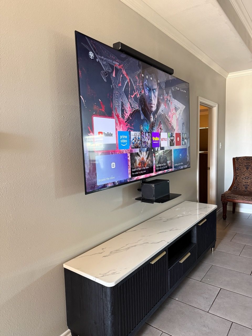 Wall-mounted TV above a white console in a modern living room with tiled floor and open doorway.