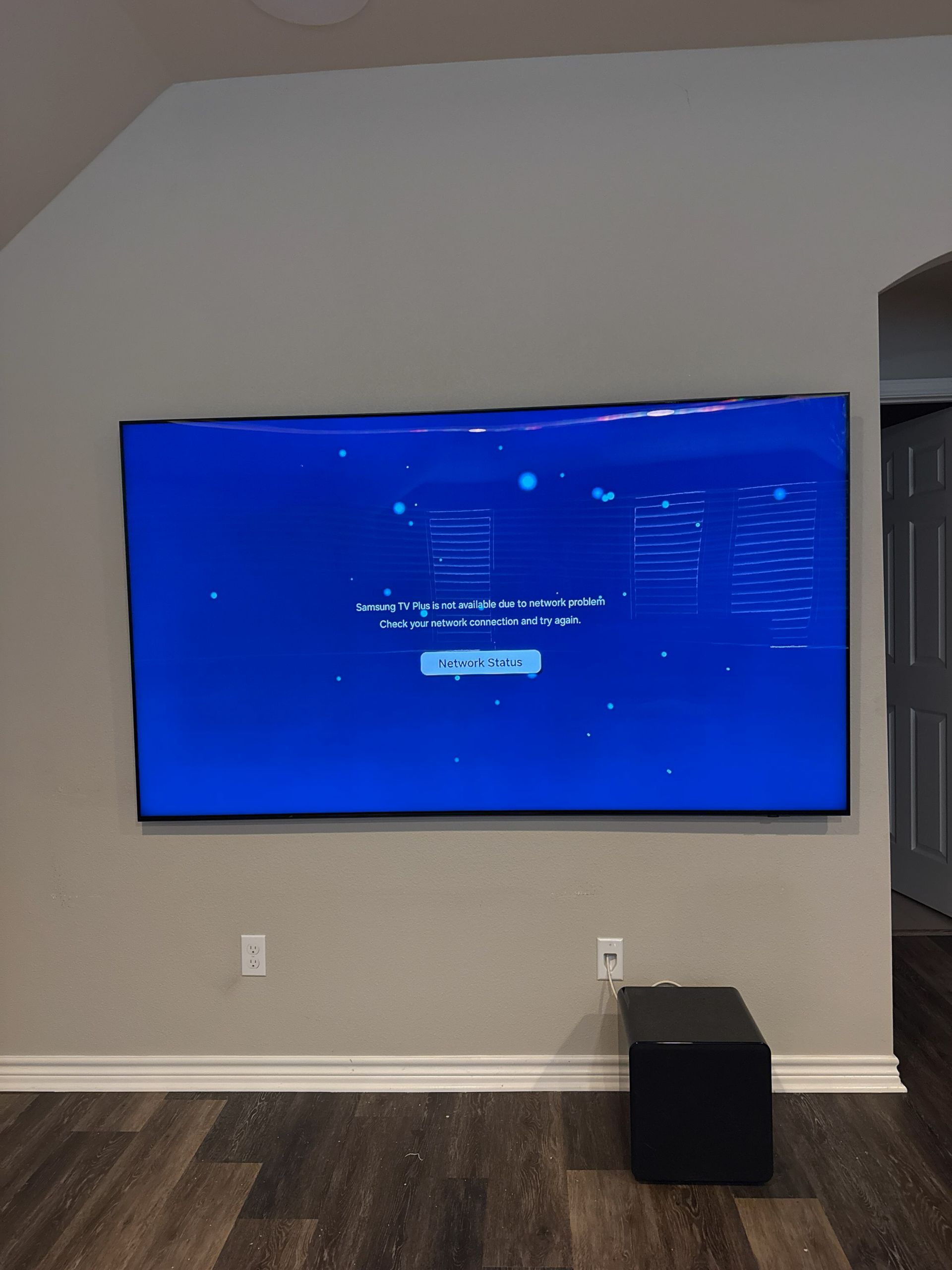 Wall-mounted TV showing a blue screen in a living room with a dark ottoman below.