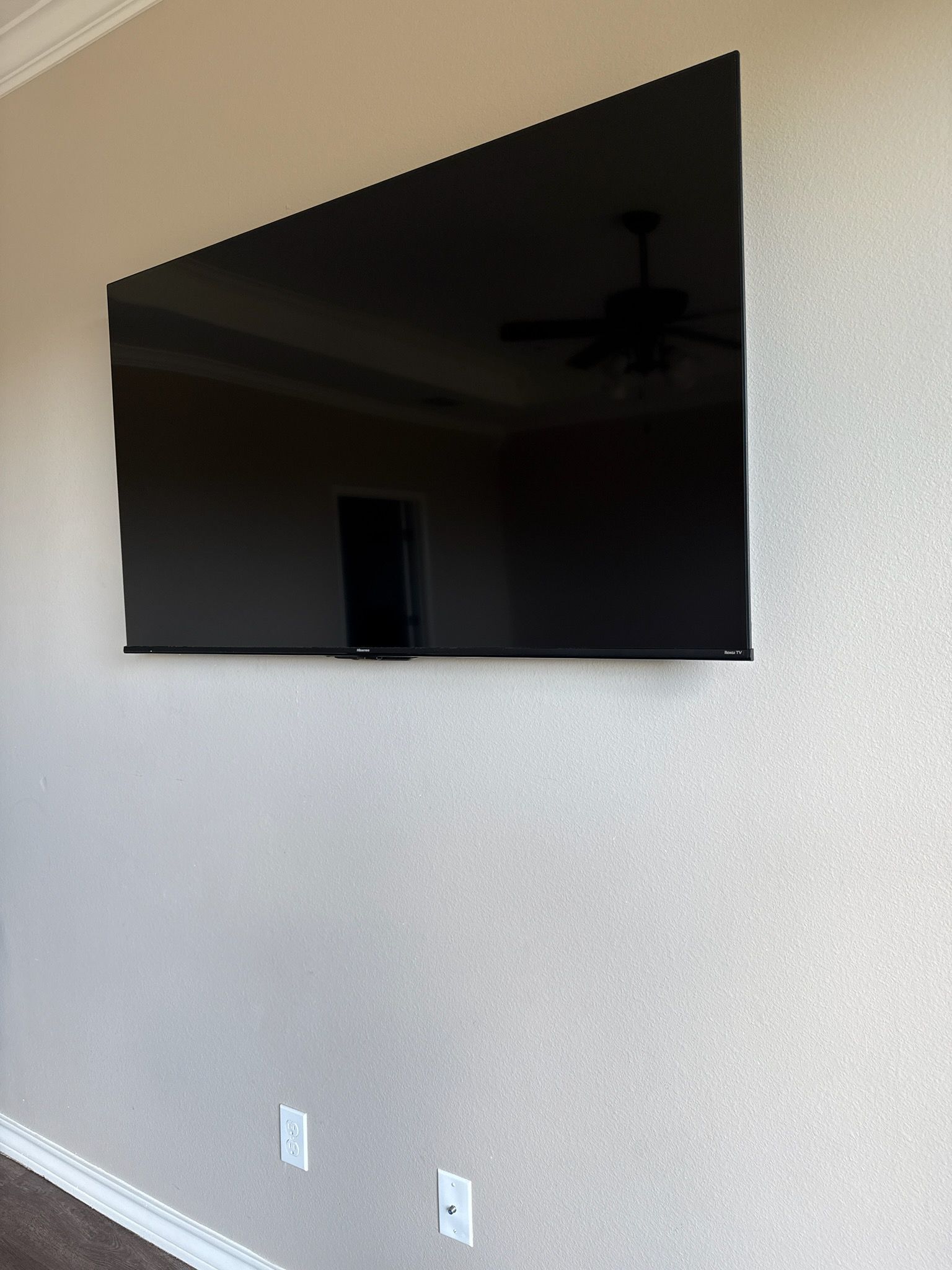 Wall-mounted black flat-screen TV on a light textured wall above two outlets.