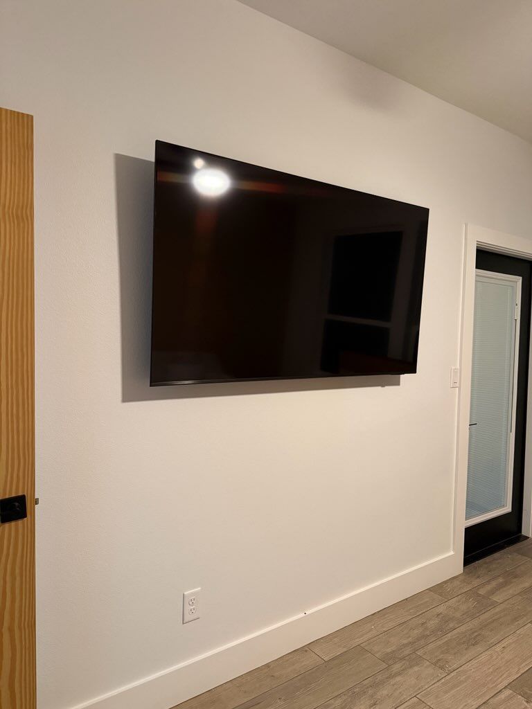 Wall-mounted flat-screen TV on a white wall in a room with beige carpet and a doorway.