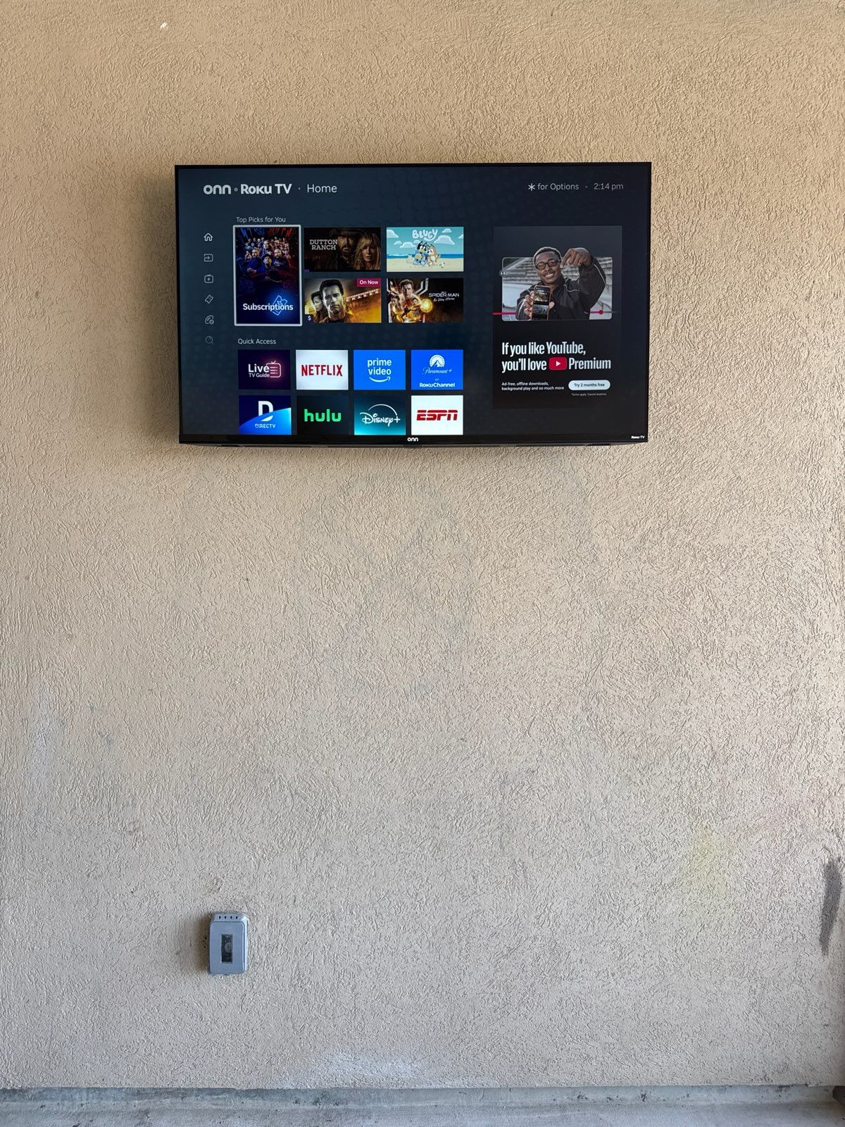 Wall-mounted TV displaying a streaming menu above a plain textured wall.