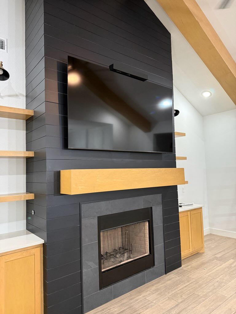 Modern living room wall with mounted TV above a black fireplace and light wood mantel shelves
