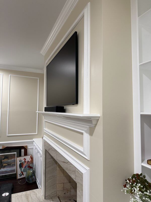 Living room fireplace with white mantel and molding, mounted flat-screen TV, and framed photos nearby