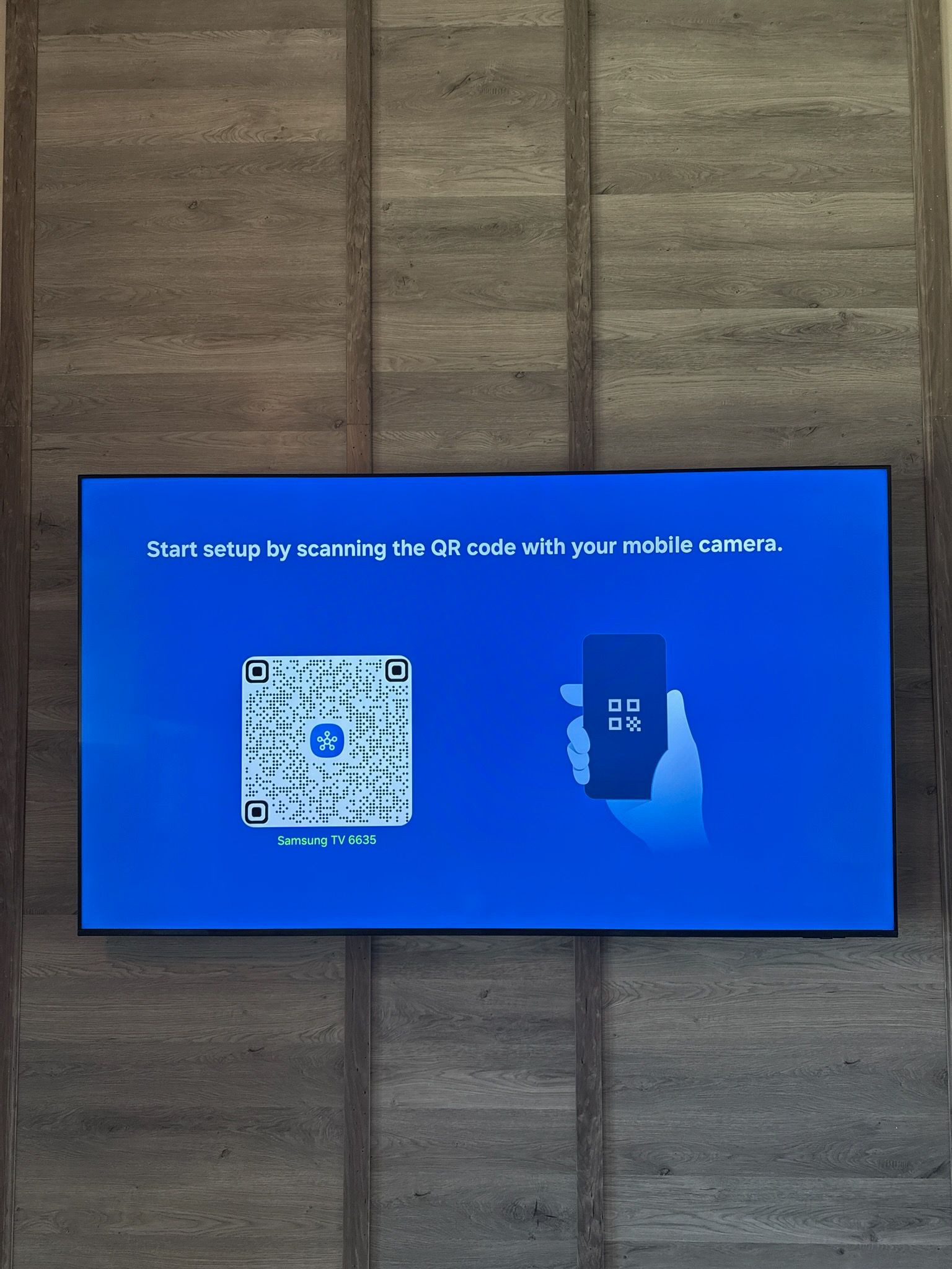 Blue TV screen with a QR code and a phone graphic on a wood-paneled wall.