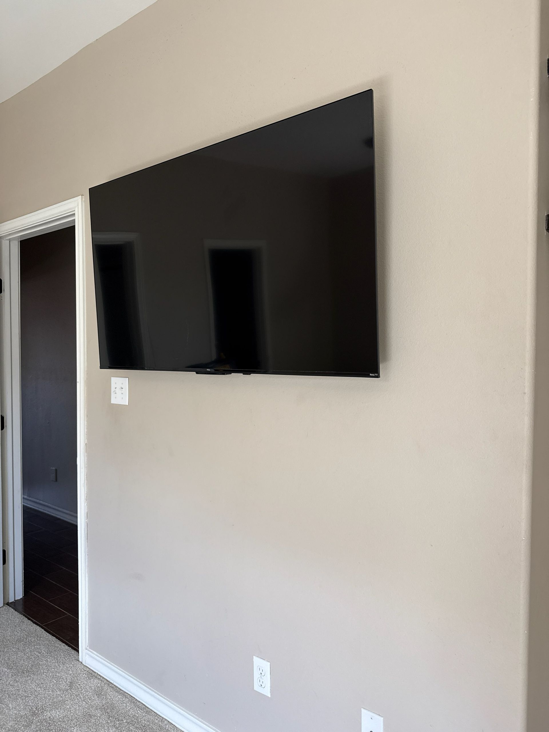 Mounted flat-screen TV on a beige wall beside a doorway in a carpeted room.
