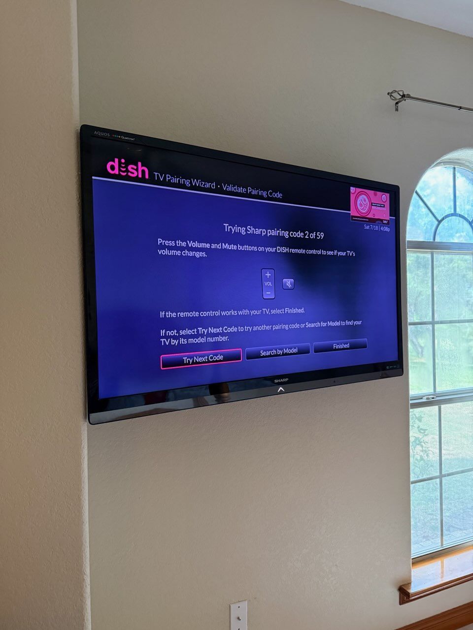 Wall-mounted TV displaying a Dish Network screen in a bright living room by an arched window.