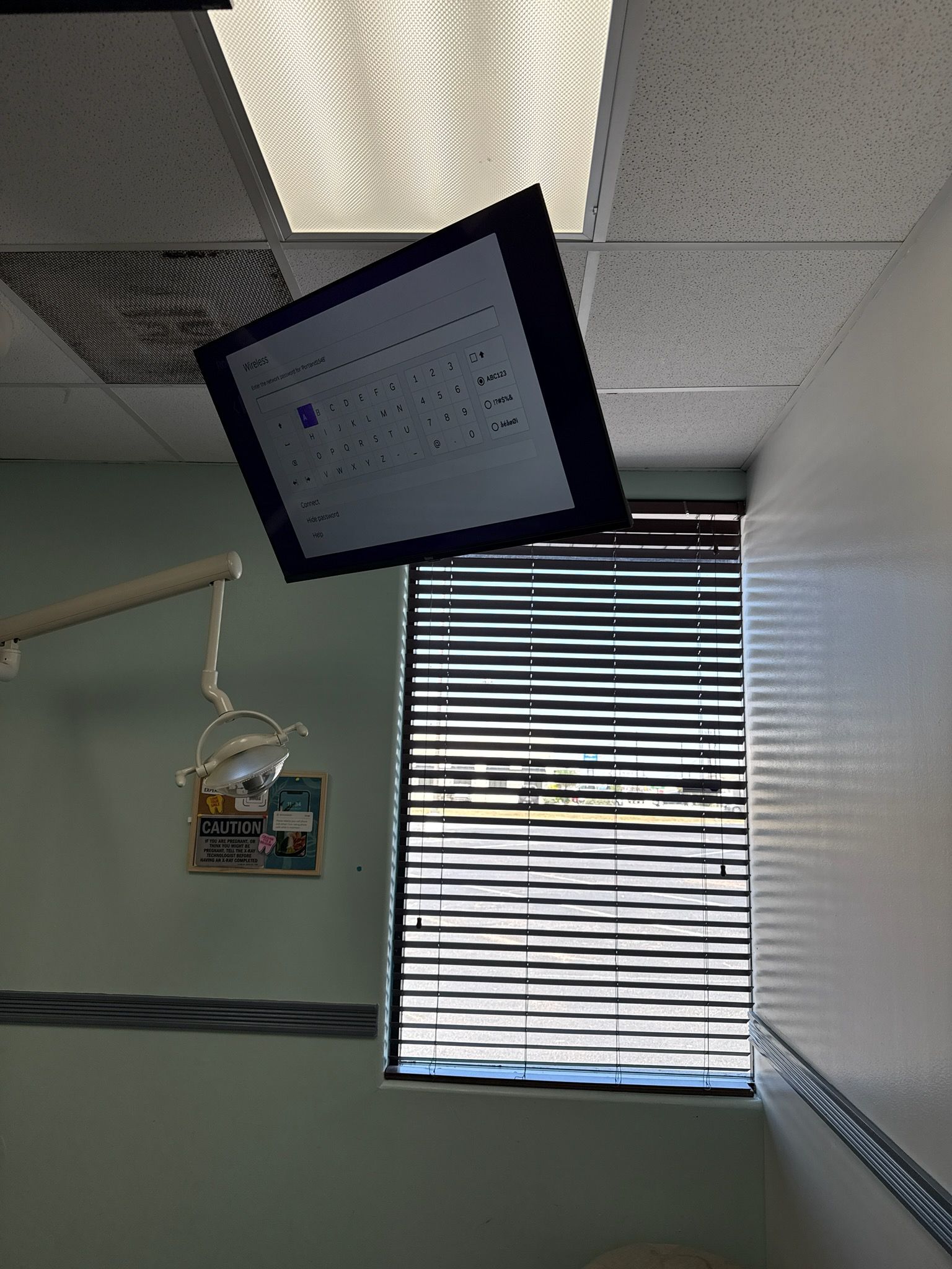 Tilted ceiling-mounted monitor in a hospital room with a window and medical equipment underneath.