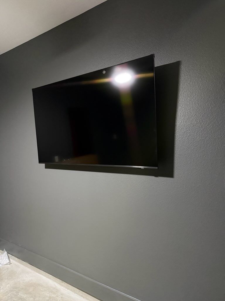 Wall-mounted flat-screen TV on a dark gray wall in a minimalist room, with light reflecting on the screen