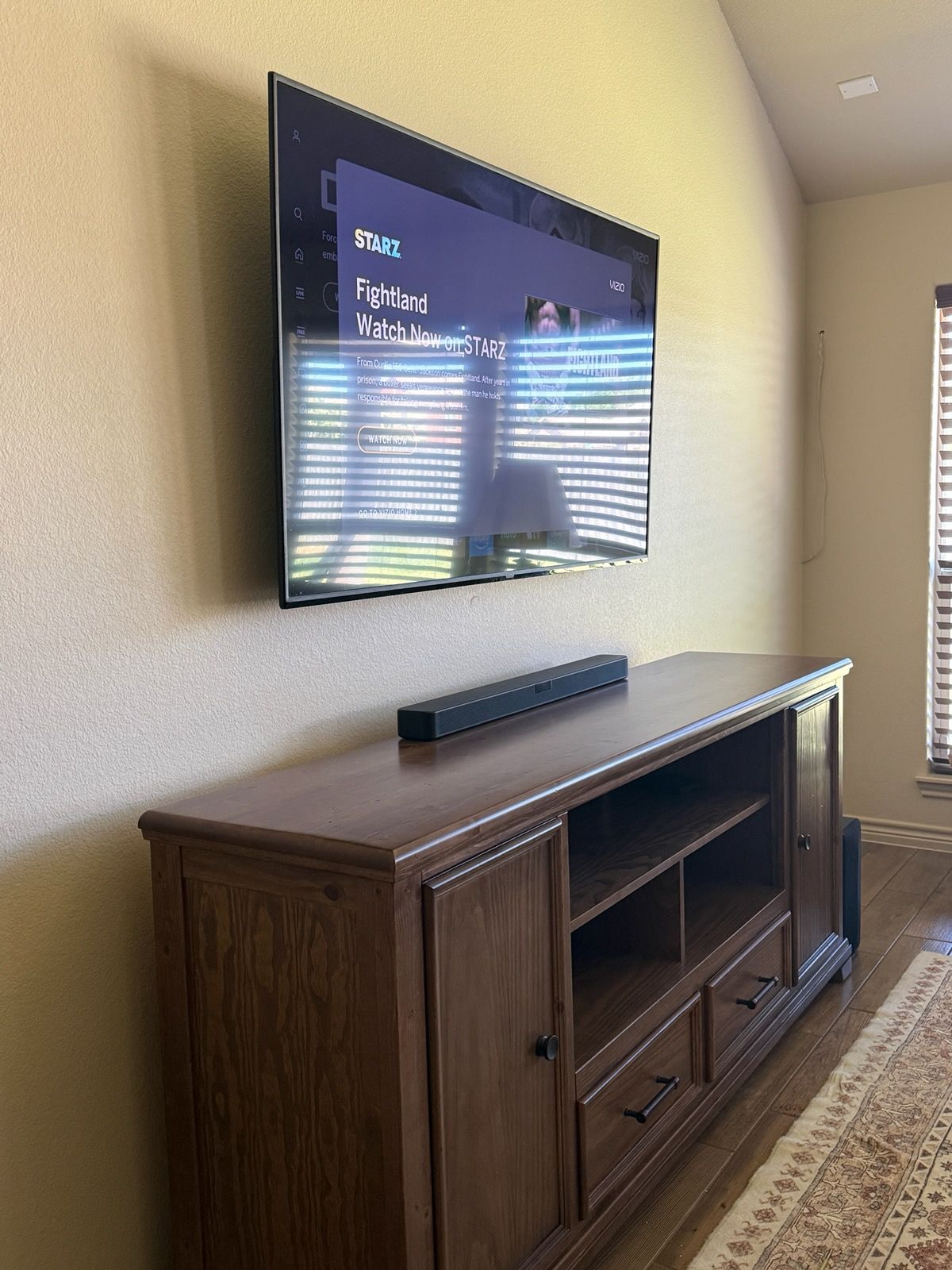 Living room with wall-mounted TV above a wooden media cabinet and soundbar by a window