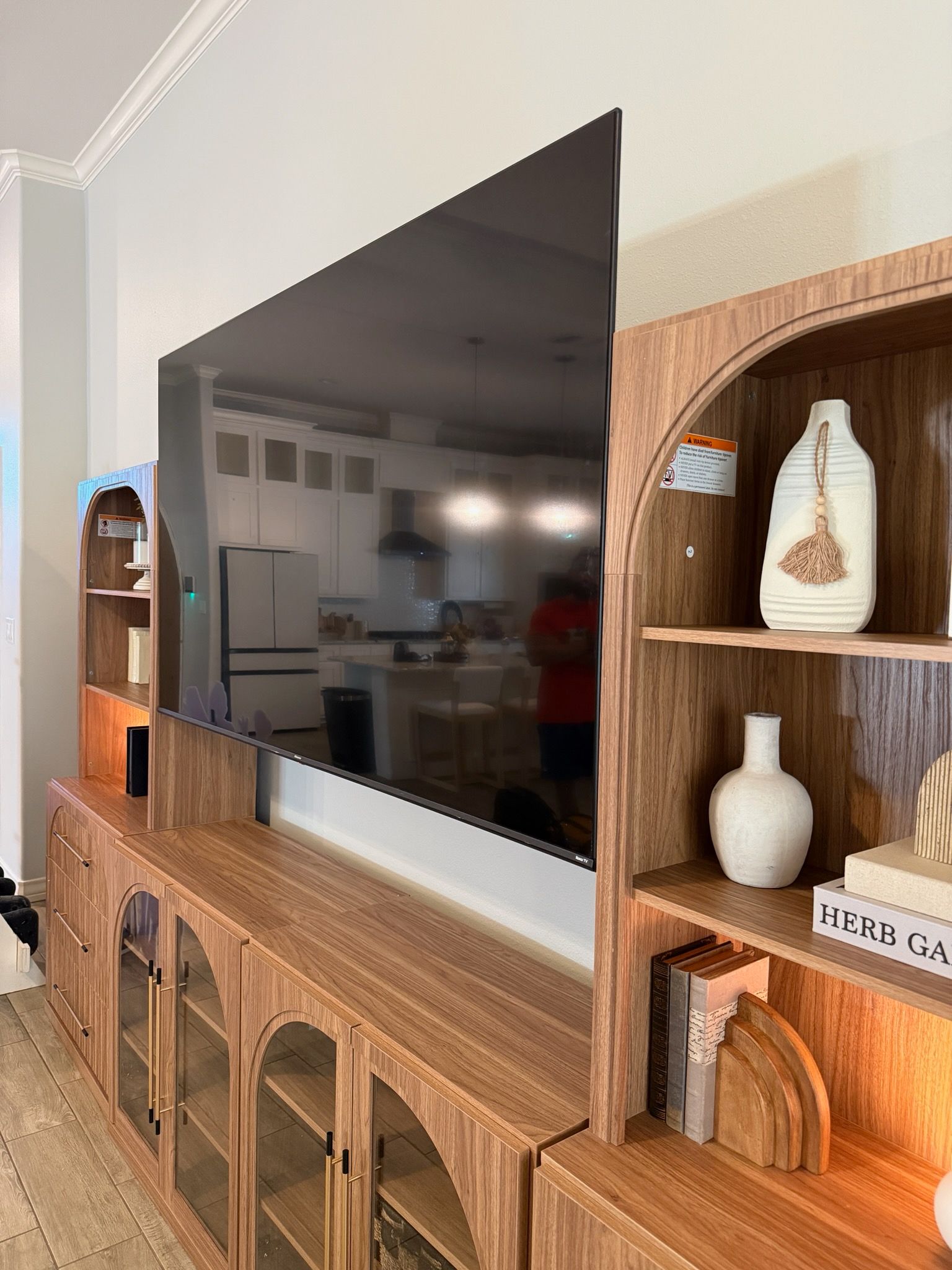 TV mounted above a wooden cabinet beside a curved wooden shelf with decor and books