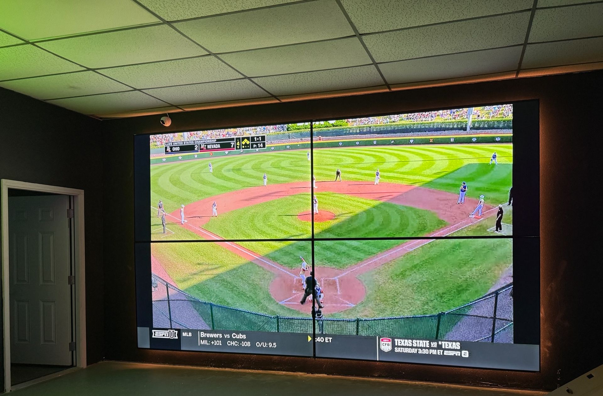 Large wall display showing a baseball game on a green field in a dark room