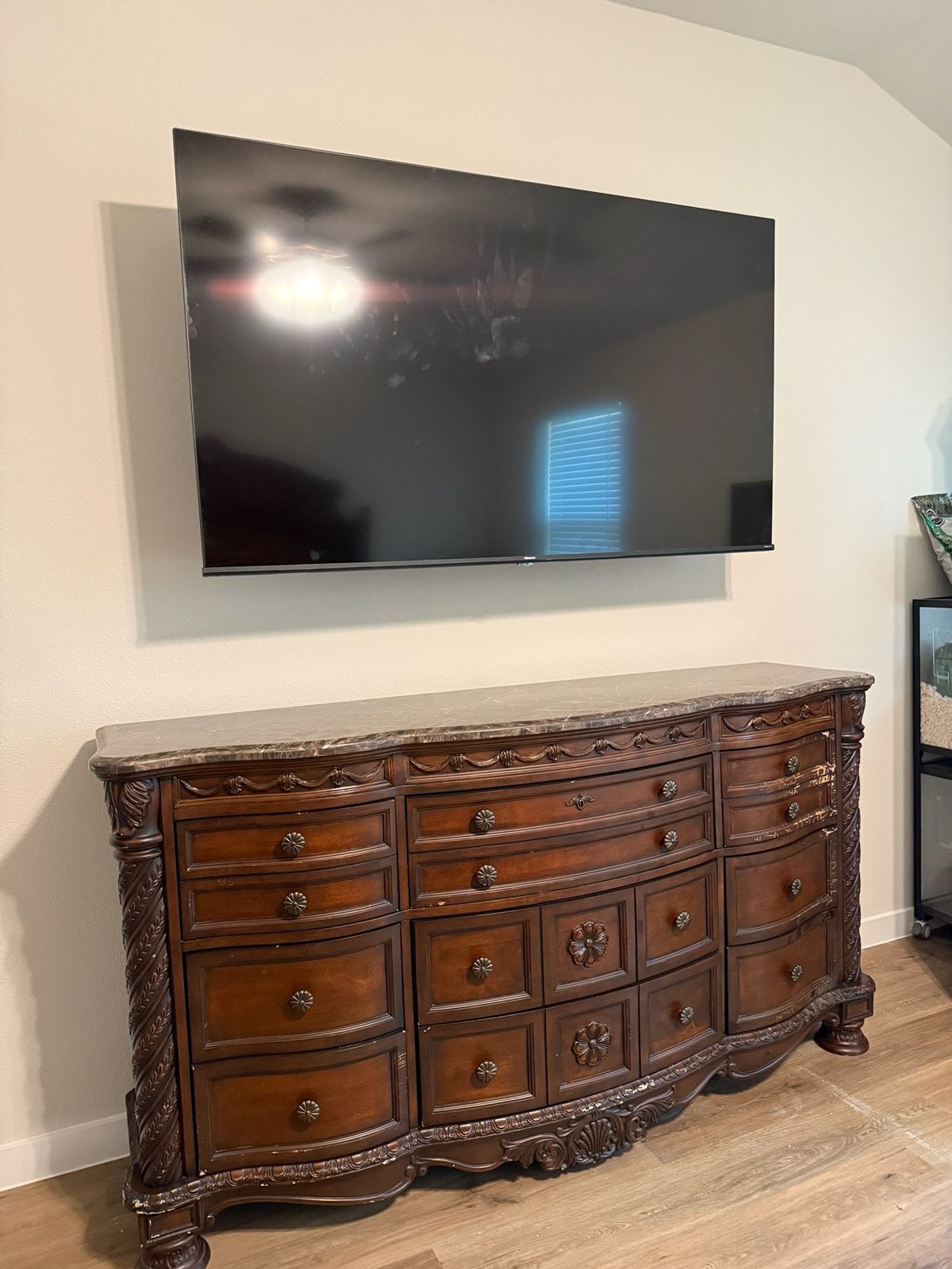 Wall-mounted TV above an ornate dark wood dresser against a light beige wall
