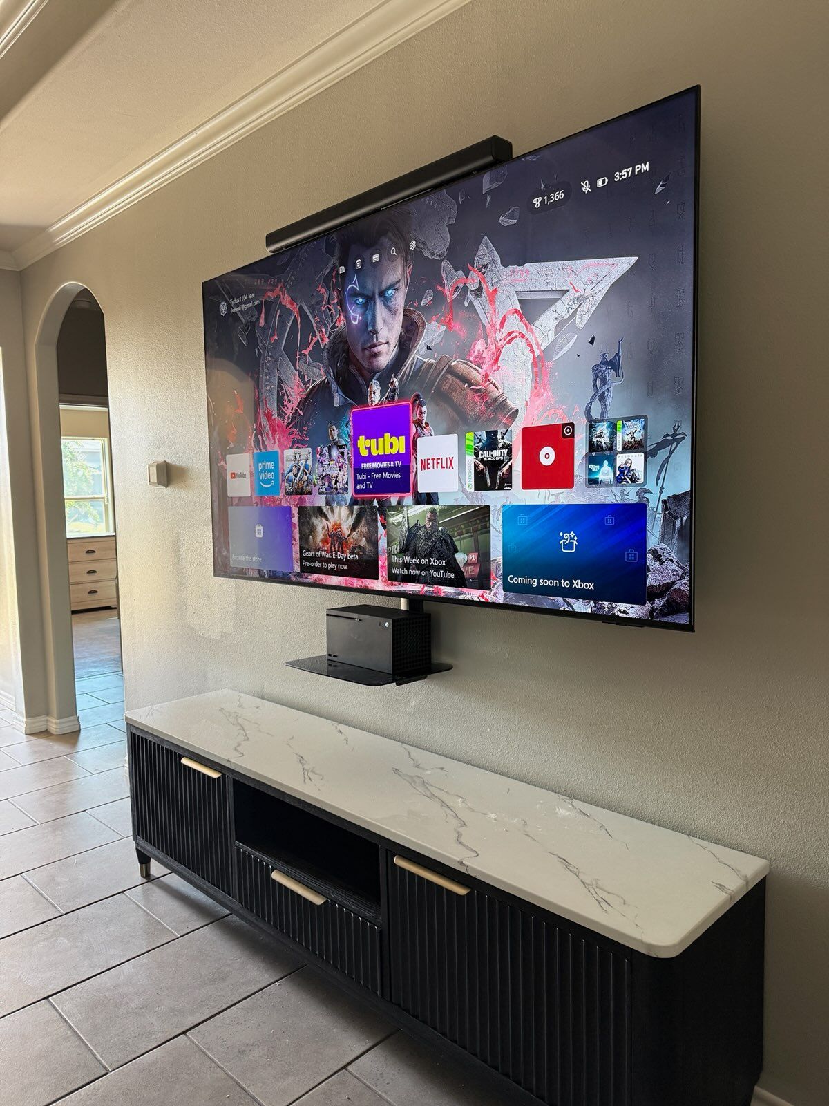 Living room TV mounted above a white console, displaying a colorful game menu