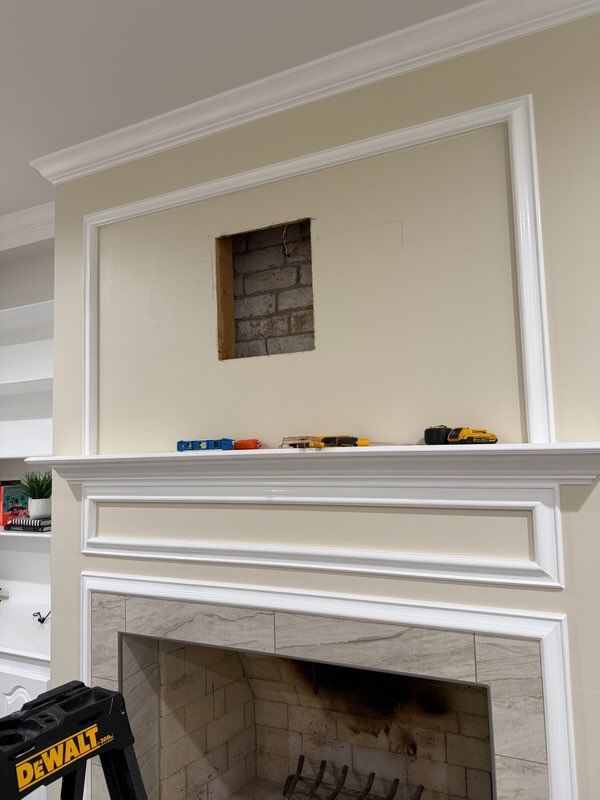 White fireplace with mantel and beige wall; square wall opening above the mantle in a room under renovation