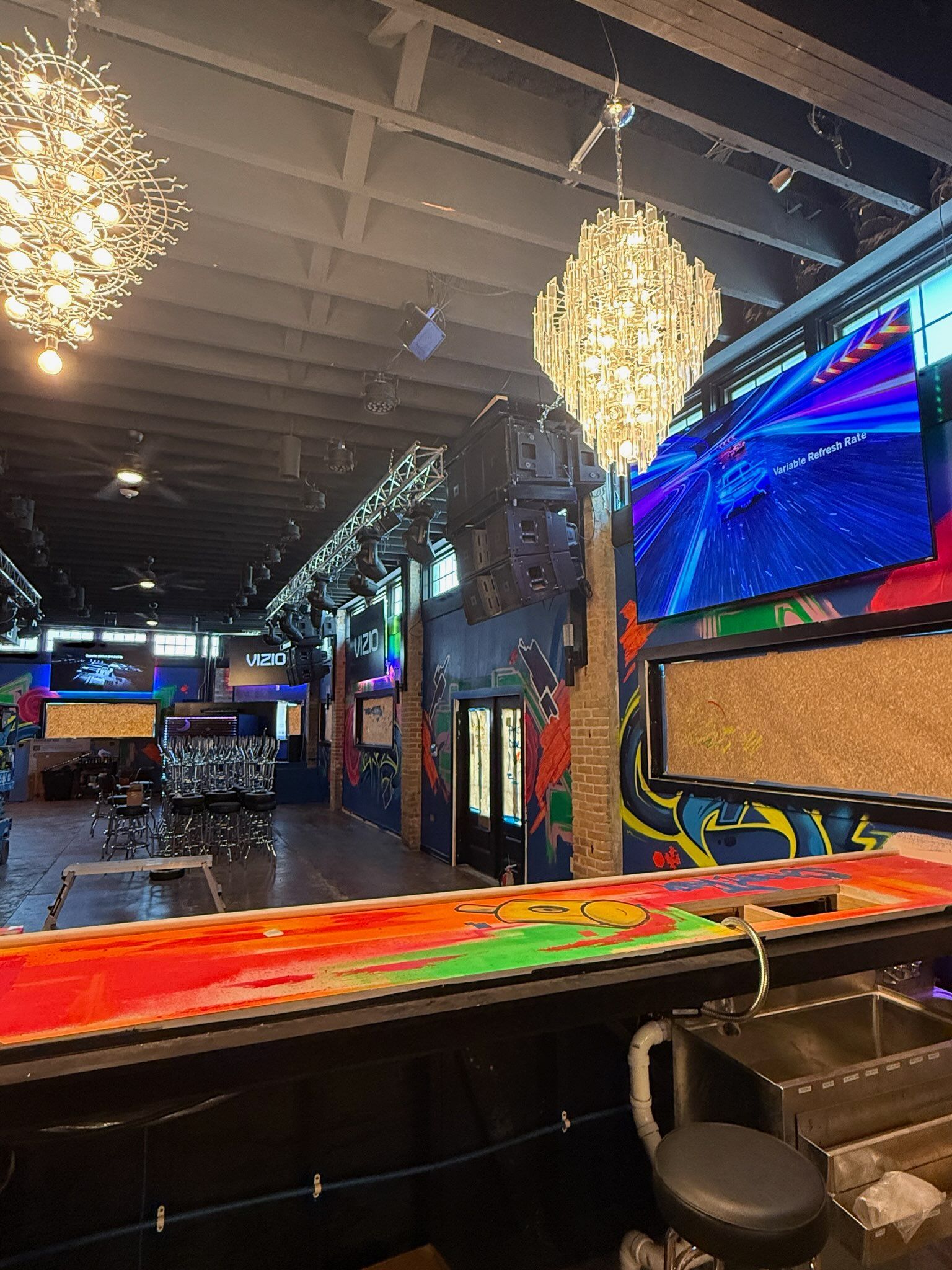 Colorful empty nightclub interior with chandeliers, neon lights, bar seating, and large screens