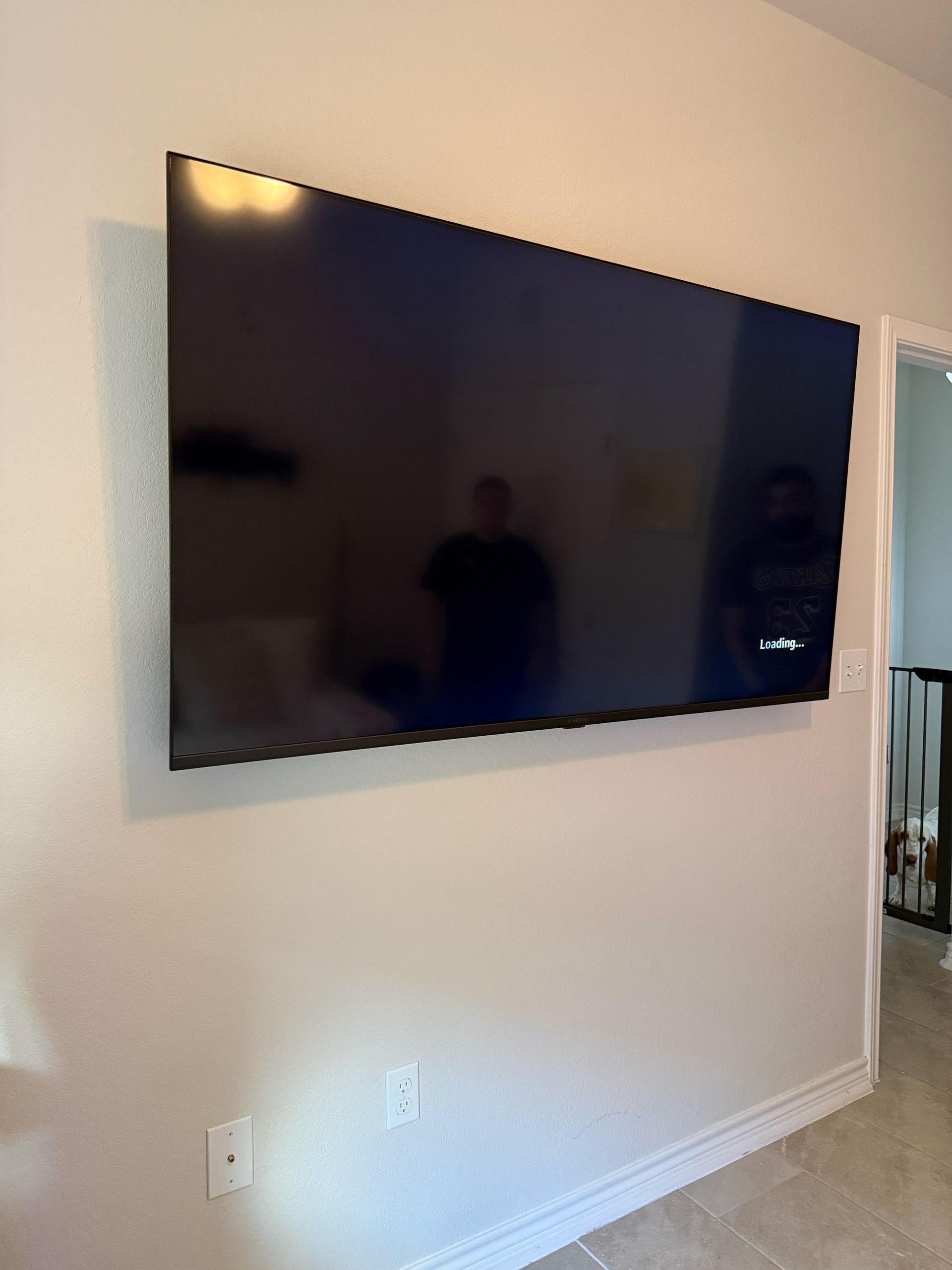 Wall-mounted flat-screen TV on a beige living room wall, above white baseboards and carpet.