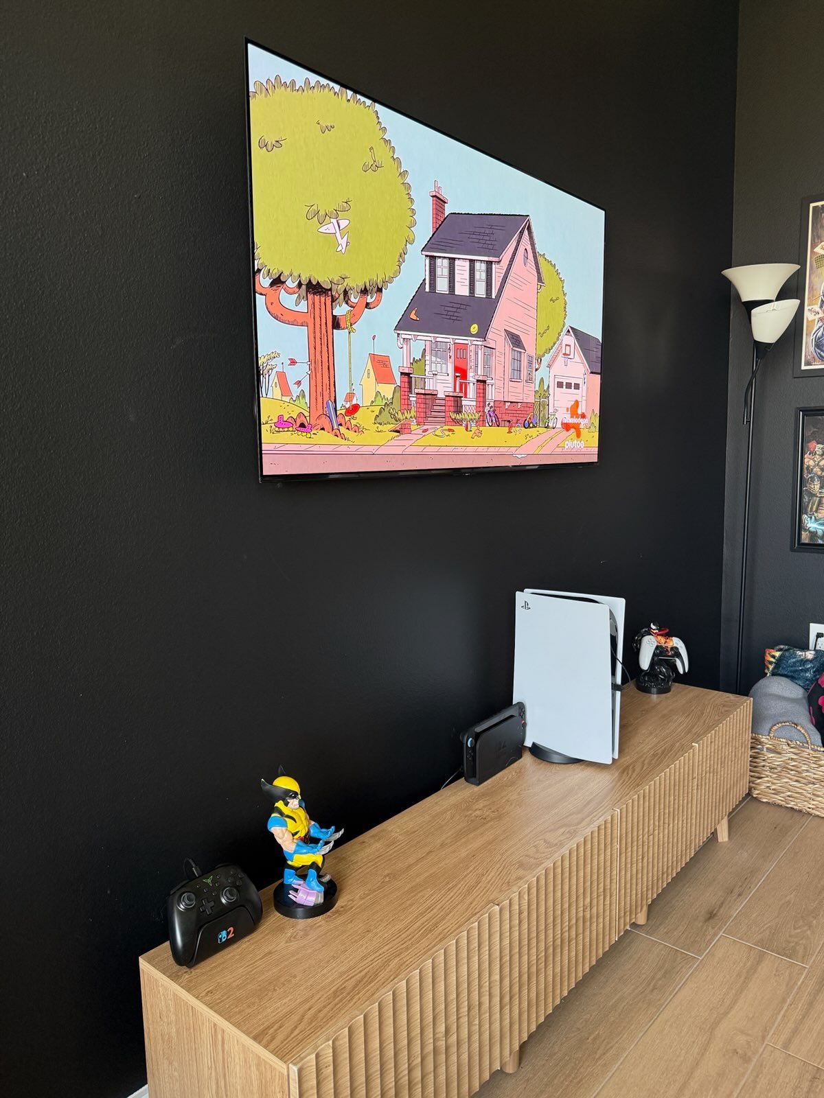 Black wall with colorful house-and-tree painting above a wicker console and small figurines