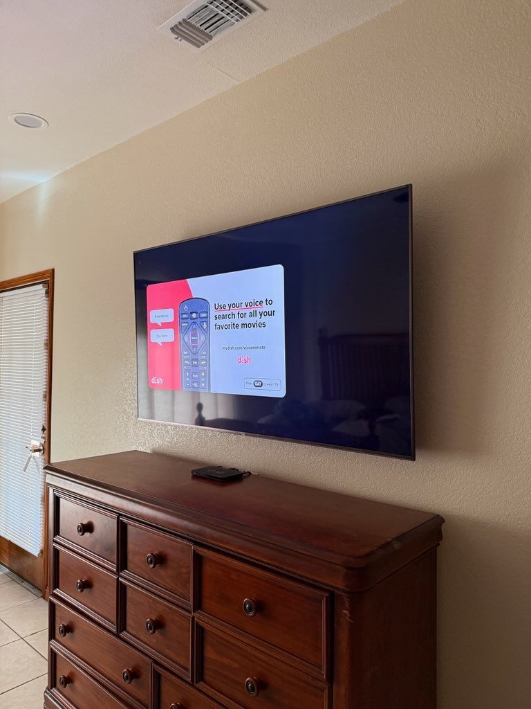 Wall-mounted TV displaying a menu above a wooden dresser in a beige bedroom