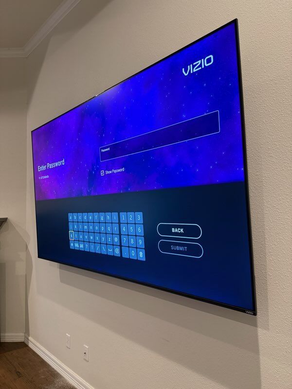 Wall-mounted Vizio TV showing a purple setup screen with an on-screen keyboard and buttons for Back and Enter.