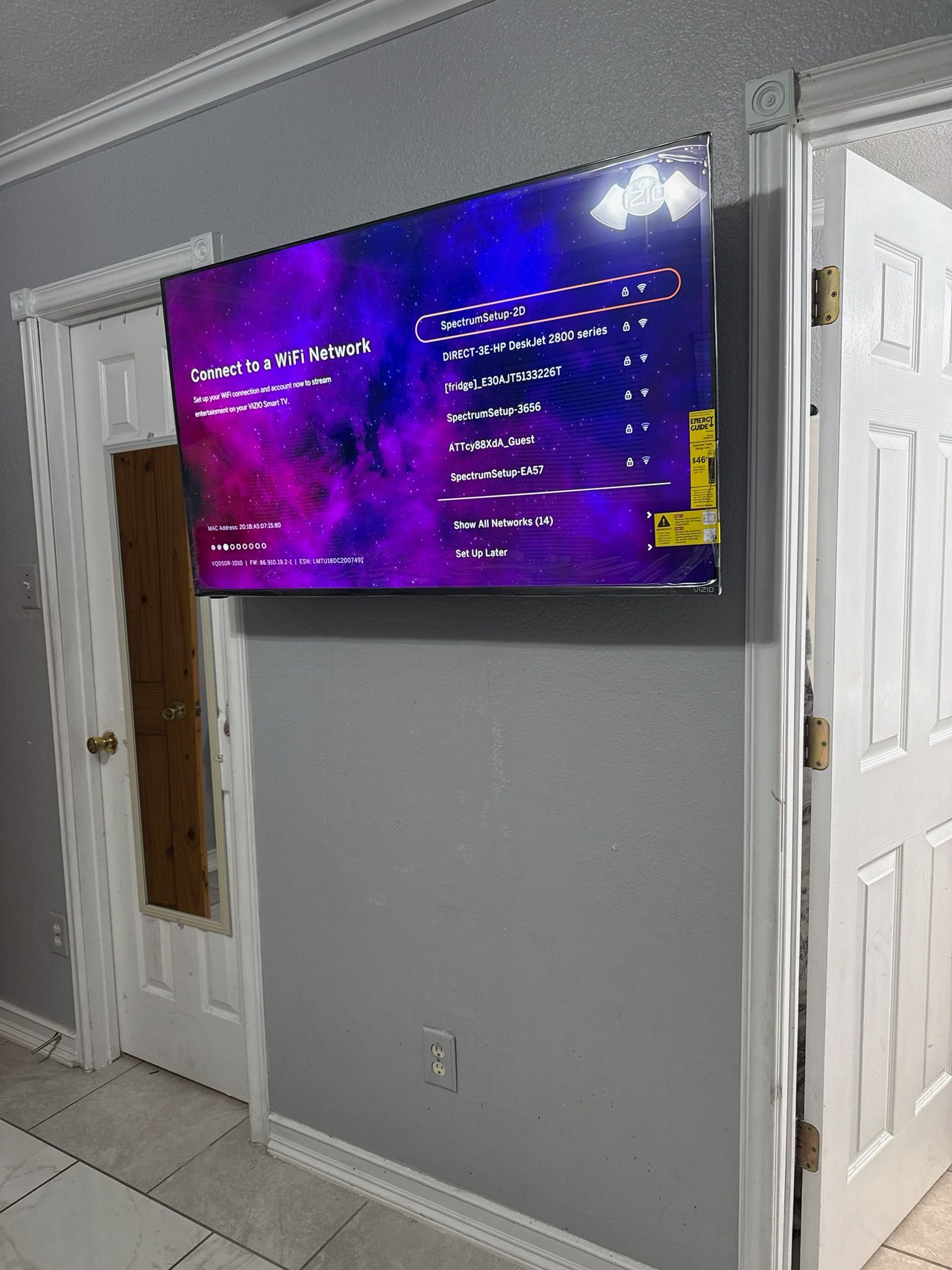 Wall-mounted TV displaying a purple menu screen in a gray hallway beside white doors