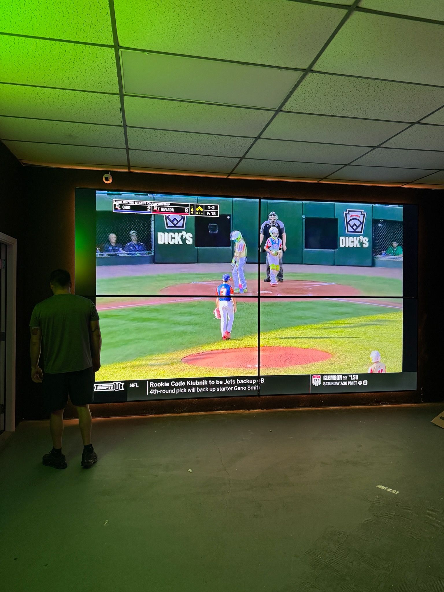 Person standing in a dark room watching a baseball game on a large indoor screen
