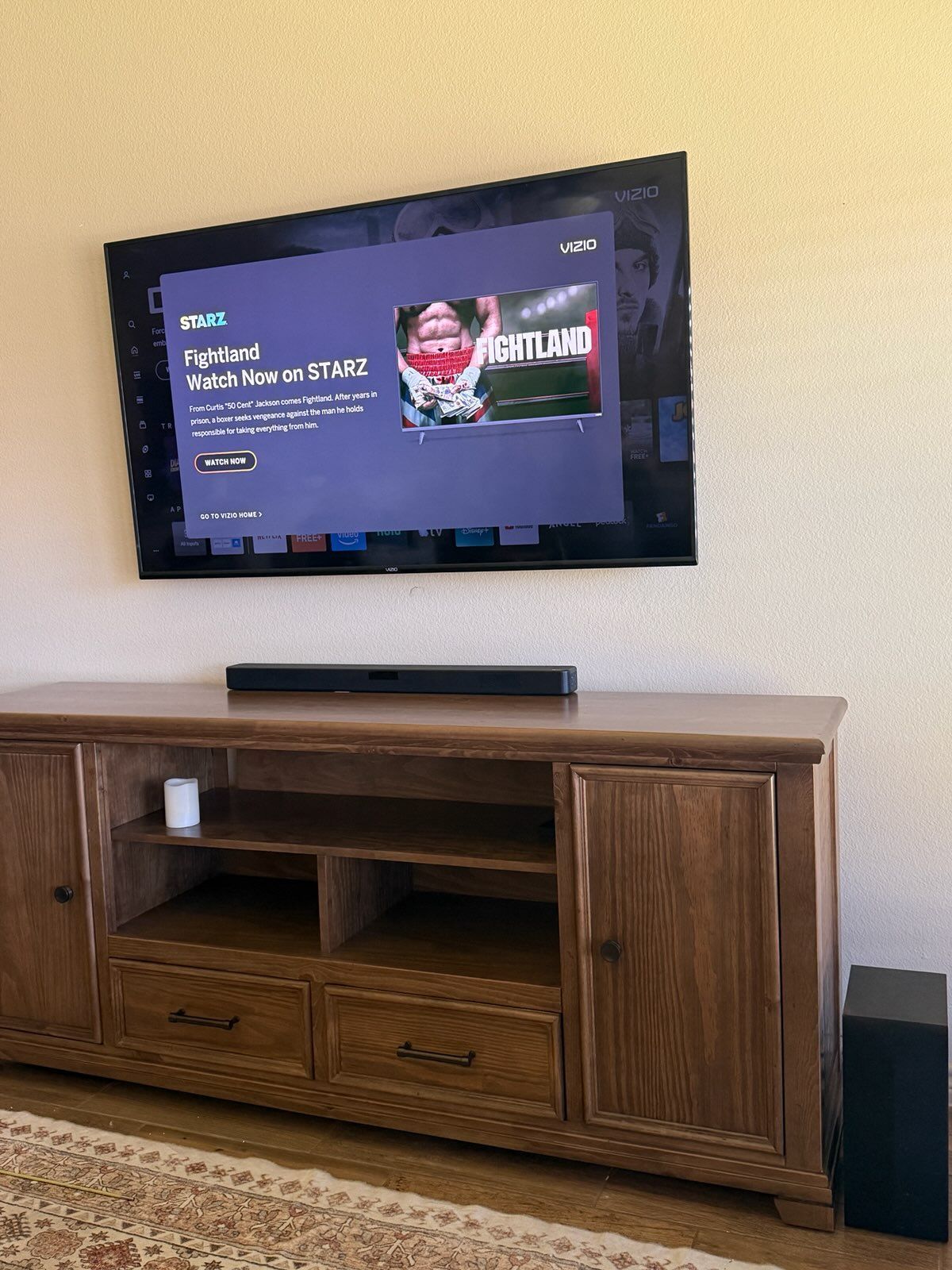 Wall-mounted TV on a wooden media console in a living room, showing a streaming home screen.