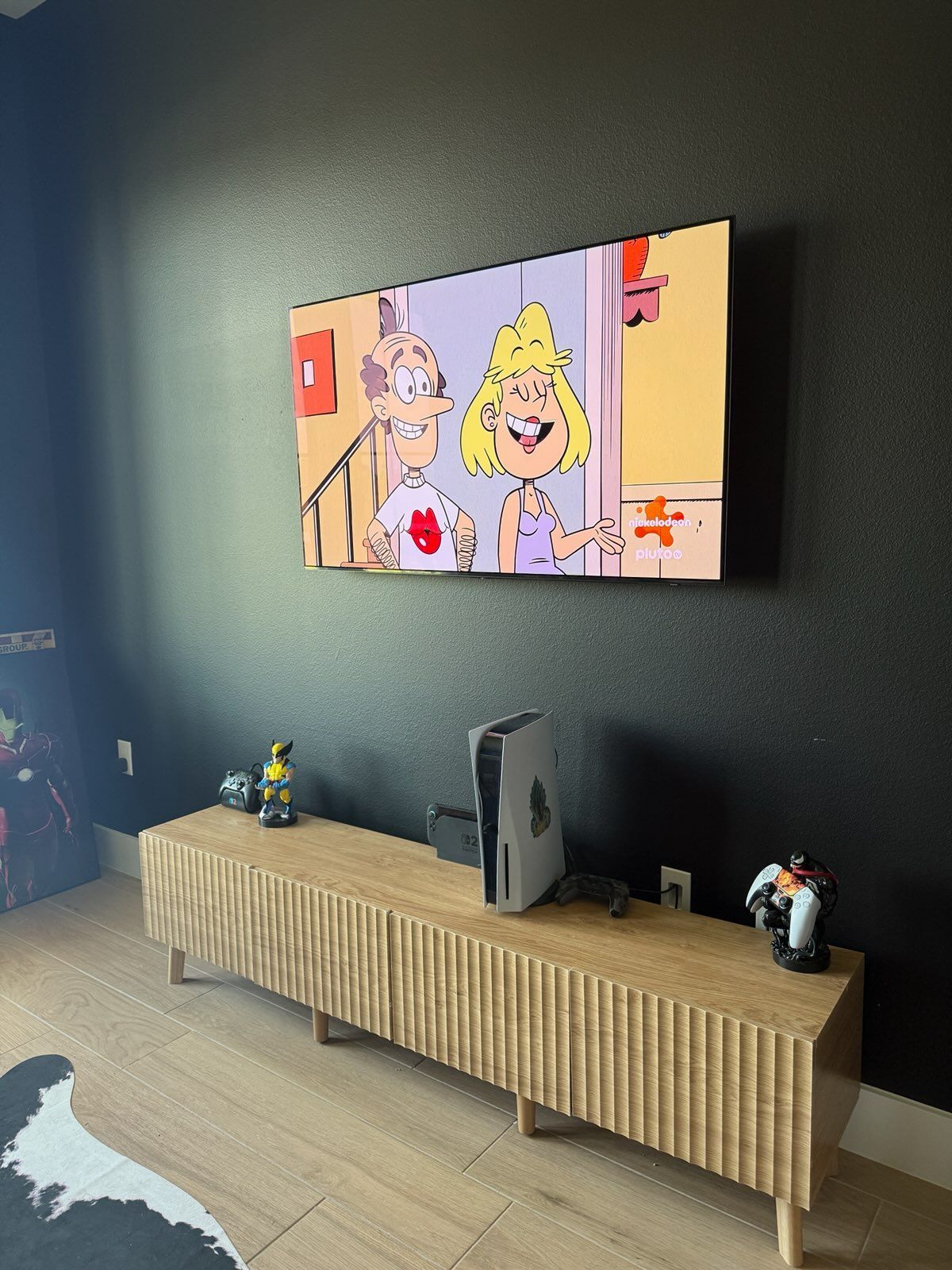 Wall-mounted TV showing a cartoon, above a long wooden media console in a dark living room.
