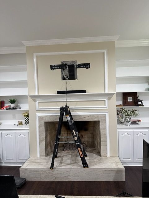 Black TV mount above empty fireplace with a ladder on the hearth in a living room