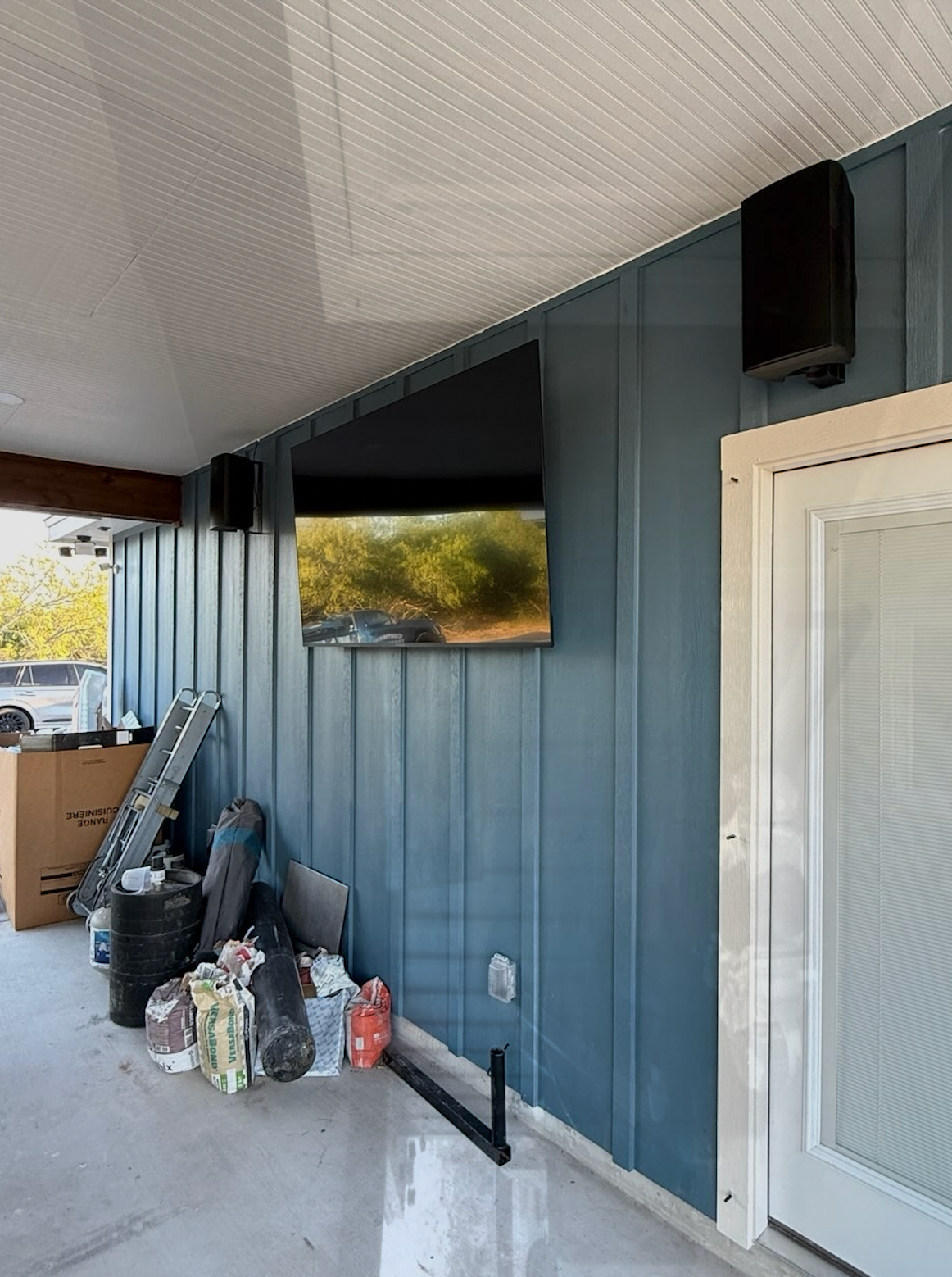 Television and speakers mounted on a blue wall of an outdoor patio.