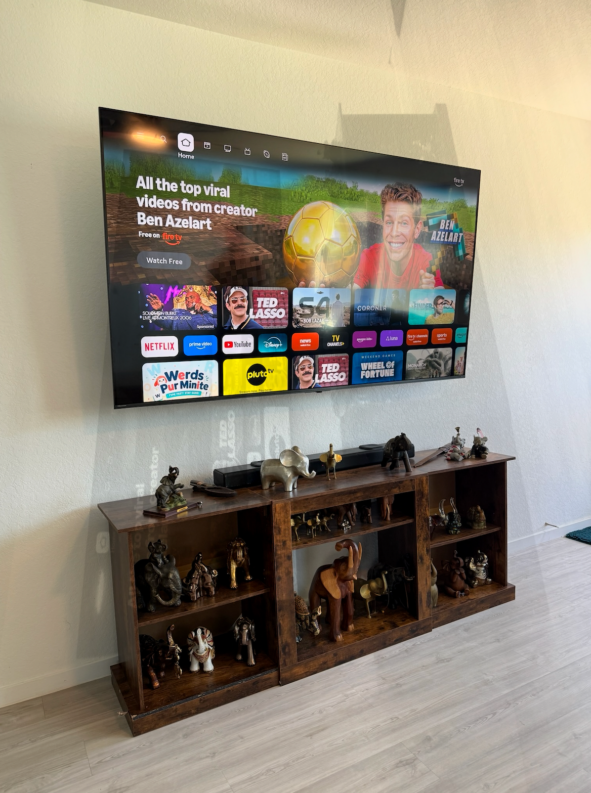 Wall-mounted TV displaying a streaming menu above a wooden cabinet with figurines in a living room.