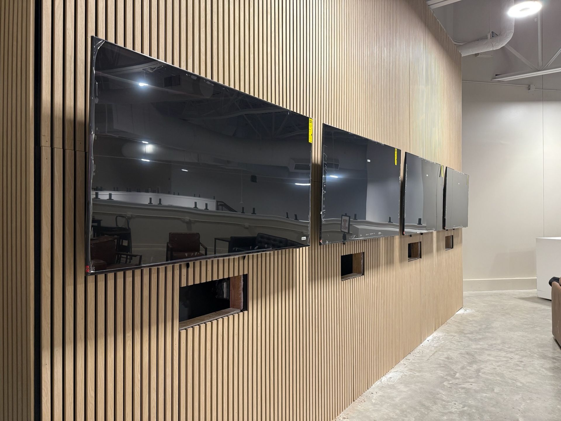 Several black flat-screen TVs mounted on a light wood-paneled wall.