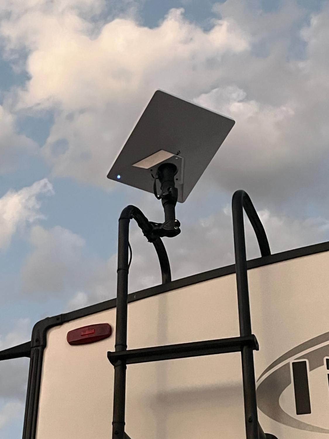 Solar panel mounted on a black RV ladder against a cloudy sky.