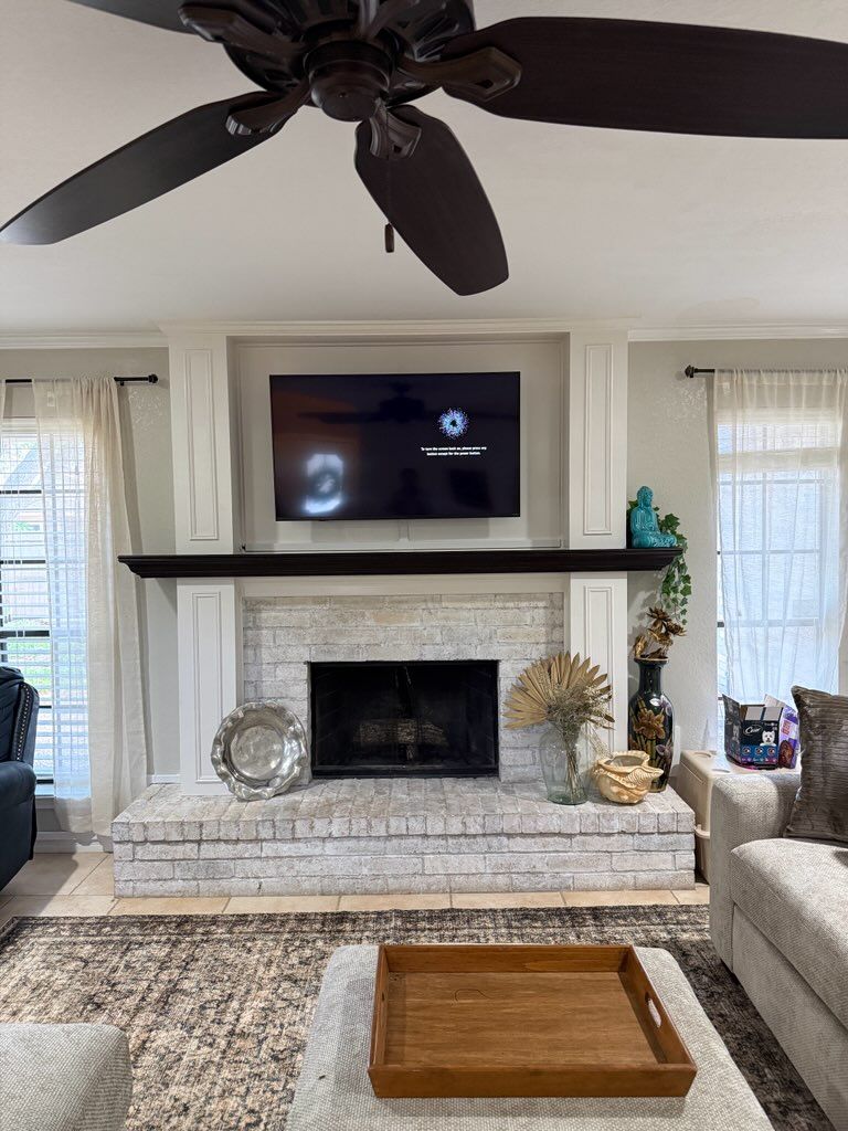 A fireplace with a white-washed brick surround and hearth, a dark wood mantel, and a flat-screen TV mounted above.