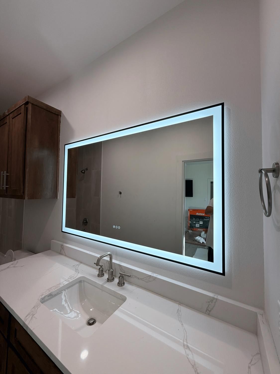 Bathroom with large, rectangular mirror with a glowing border over a white countertop and sink.