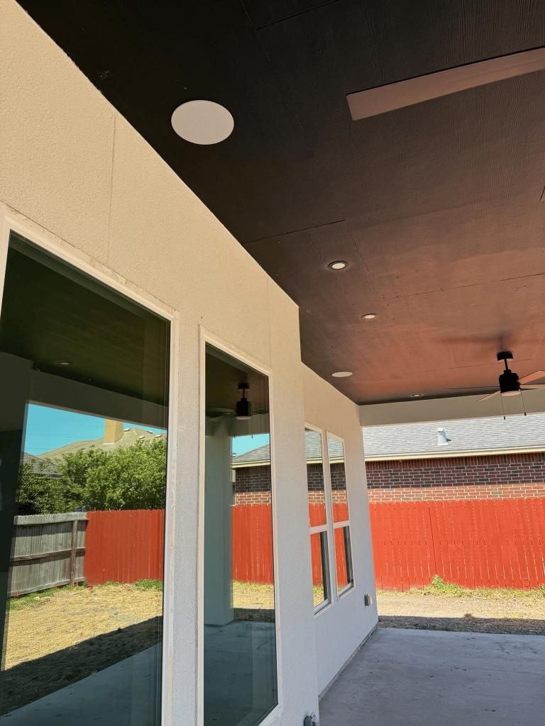 Exterior patio with a black ceiling, recessed lights, and glass windows reflecting the yard and red fence.