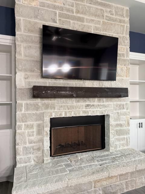Stone fireplace with TV, dark wooden mantel, and built-in white bookshelves.