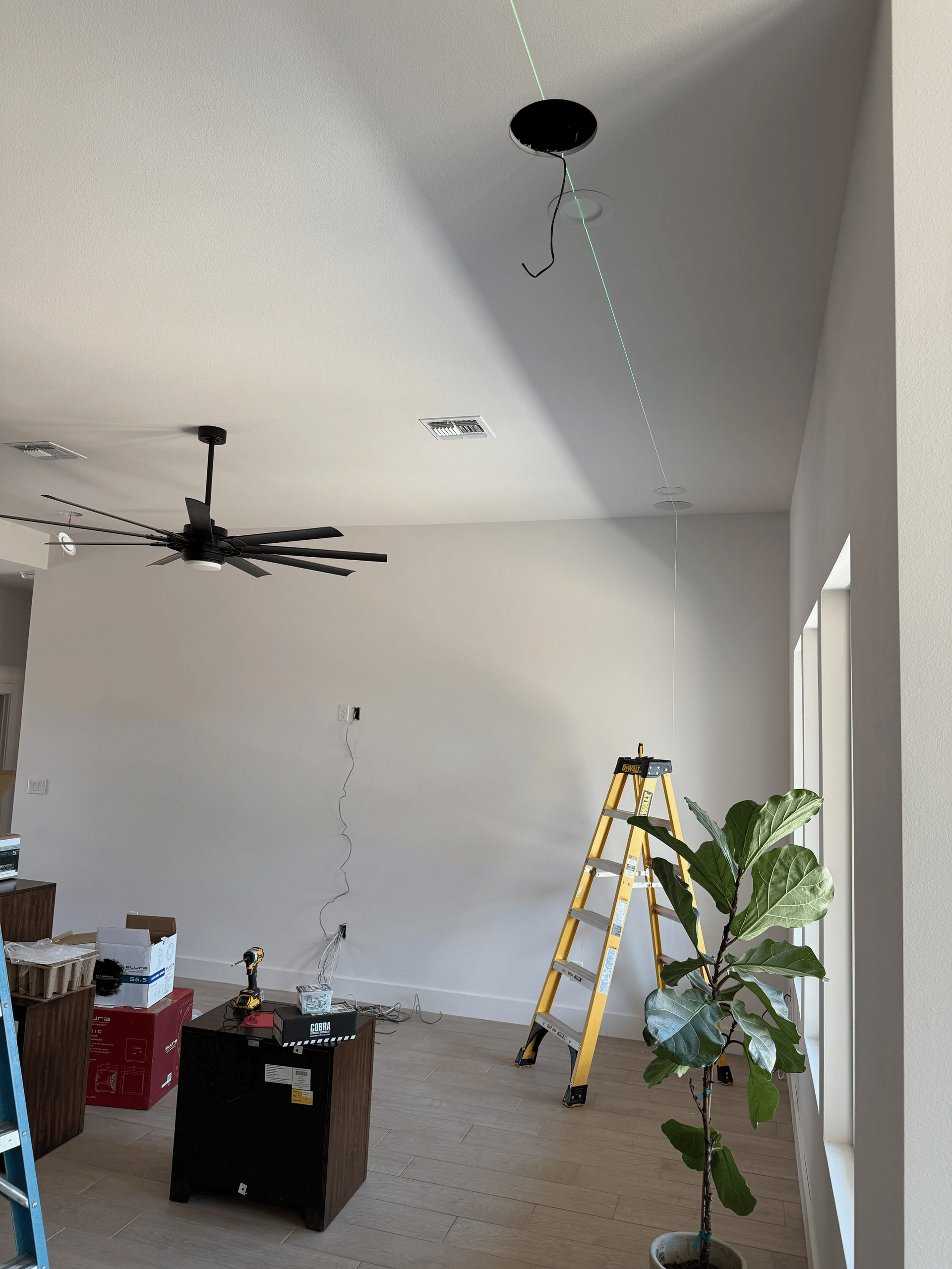 Interior room with recessed lighting holes in ceiling; ceiling fan, ladder, and plant visible.