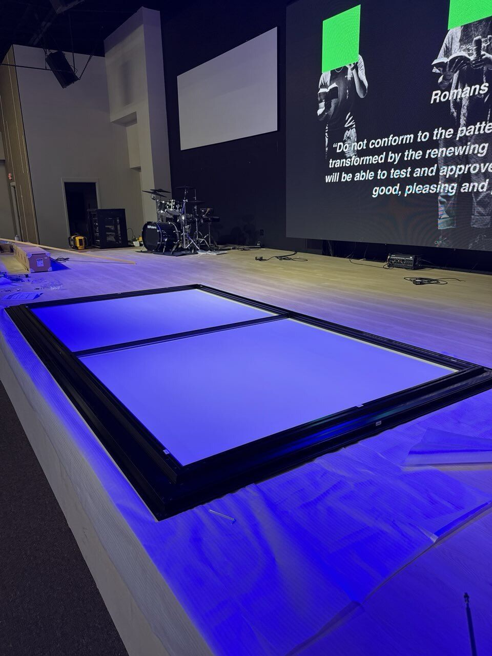 A rectangular black frame with blue glow, possibly an LED screen, on a stage with a projection screen behind it.