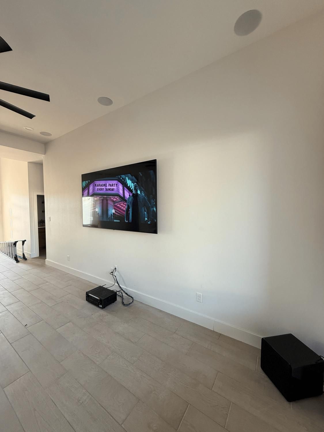 Large TV mounted on a white wall in a modern room with a projector and speaker on the floor.