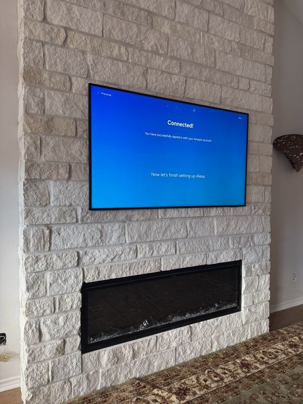 TV mounted on a white stone wall above a black fireplace, screen displaying a blue connected screen.